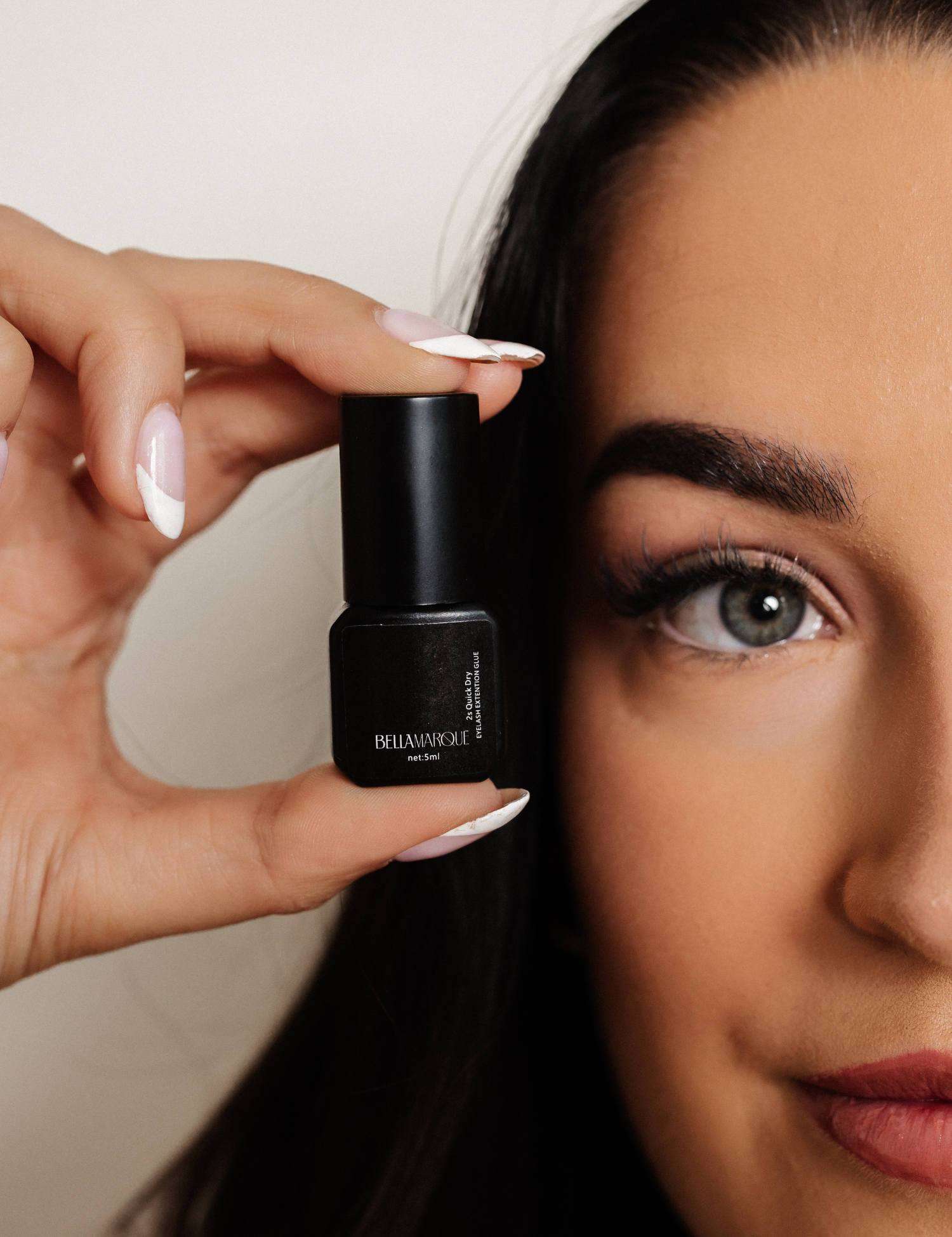 Woman holding a small bottle of Bellamarque eyelash extension glue near her face