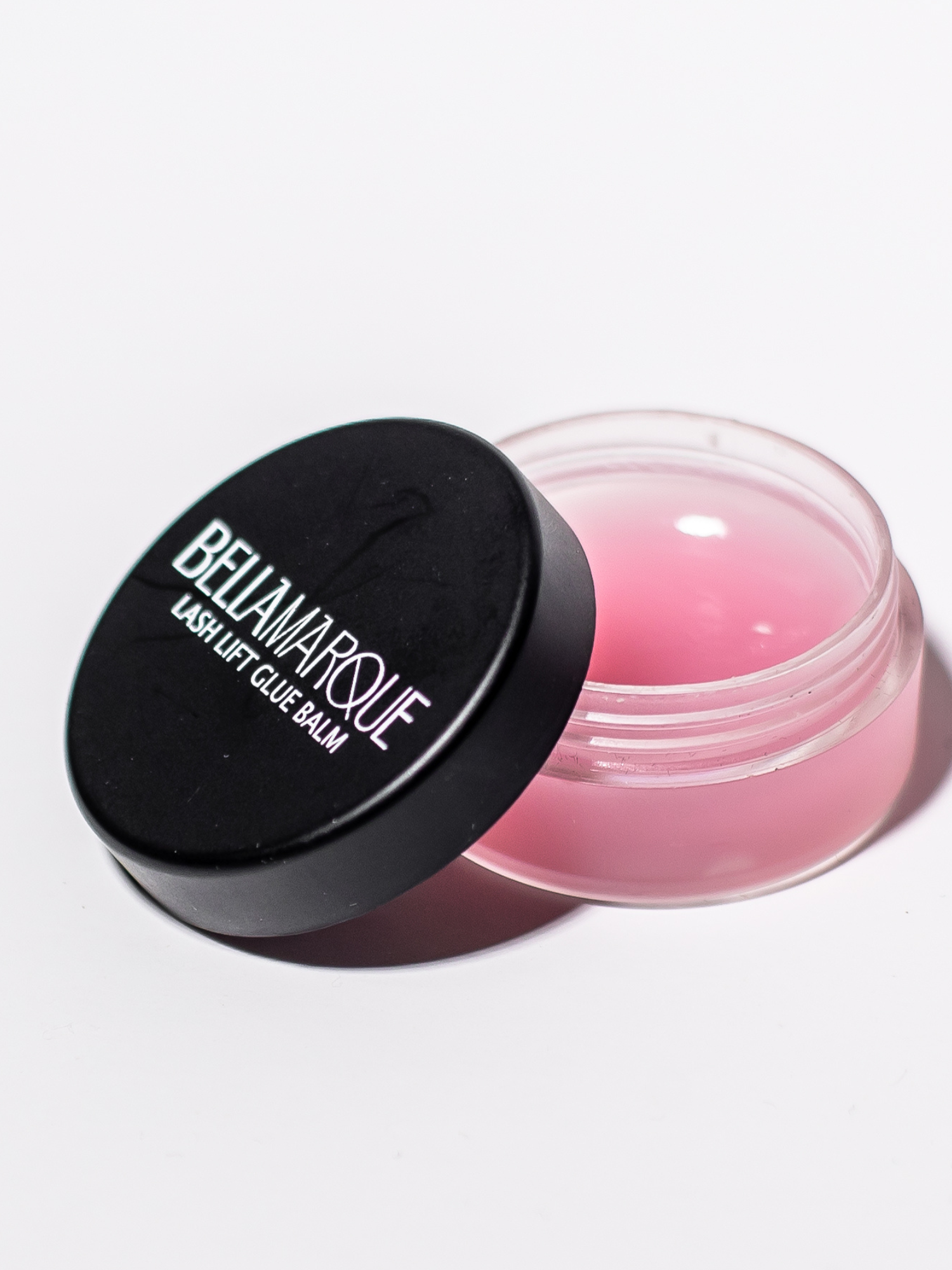 Open lash balm container on white surface