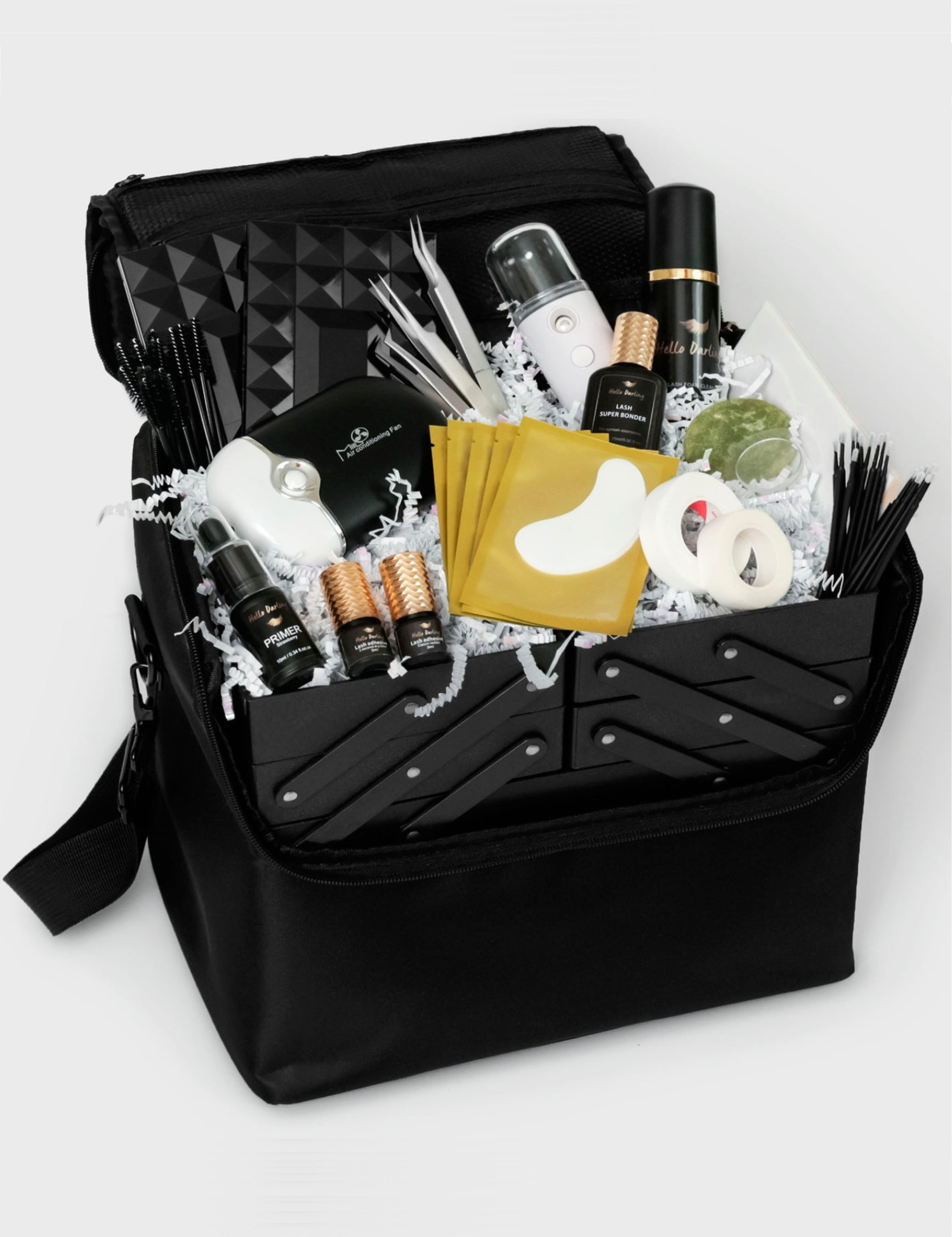 A black carry case open to reveal neatly arranged eyelash extension supplies nestled in white crinkle paper. The case includes a variety of tools such as lash cleansers in sleek bottles, lash primer, motorized fans, several boxes of lash extensions, and a pack of eye pads, organized to ensure easy access and mobility.