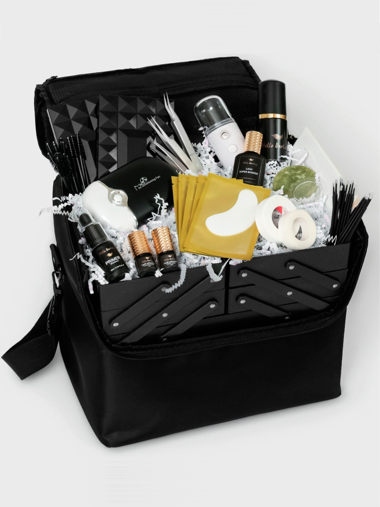 A black carry case open to reveal neatly arranged eyelash extension supplies nestled in white crinkle paper. The case includes a variety of tools such as lash cleansers in sleek bottles, lash primer, motorized fans, several boxes of lash extensions, and a pack of eye pads, organized to ensure easy access and mobility.