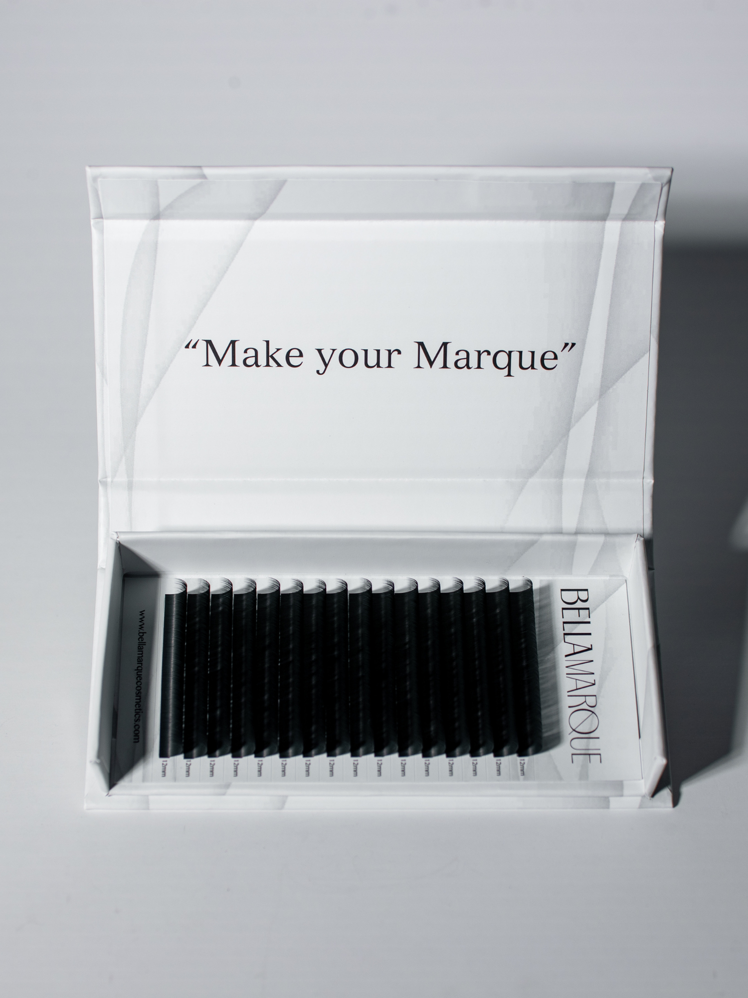 Inside view of a lash extension tray with black fibers lined up in varying lengths, under the text 'Make your Marque' printed on the upper part of the open black tray